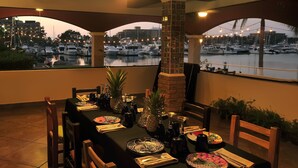 Mesa de comedor preparada para cuatro personas, con vista a un puerto deportivo y barcos.