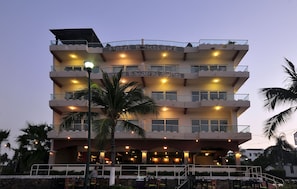 Un hotel de varios pisos con balcones, mobiliario exterior y un cartel que dice "Hotel Boutique La Bandera Suites".