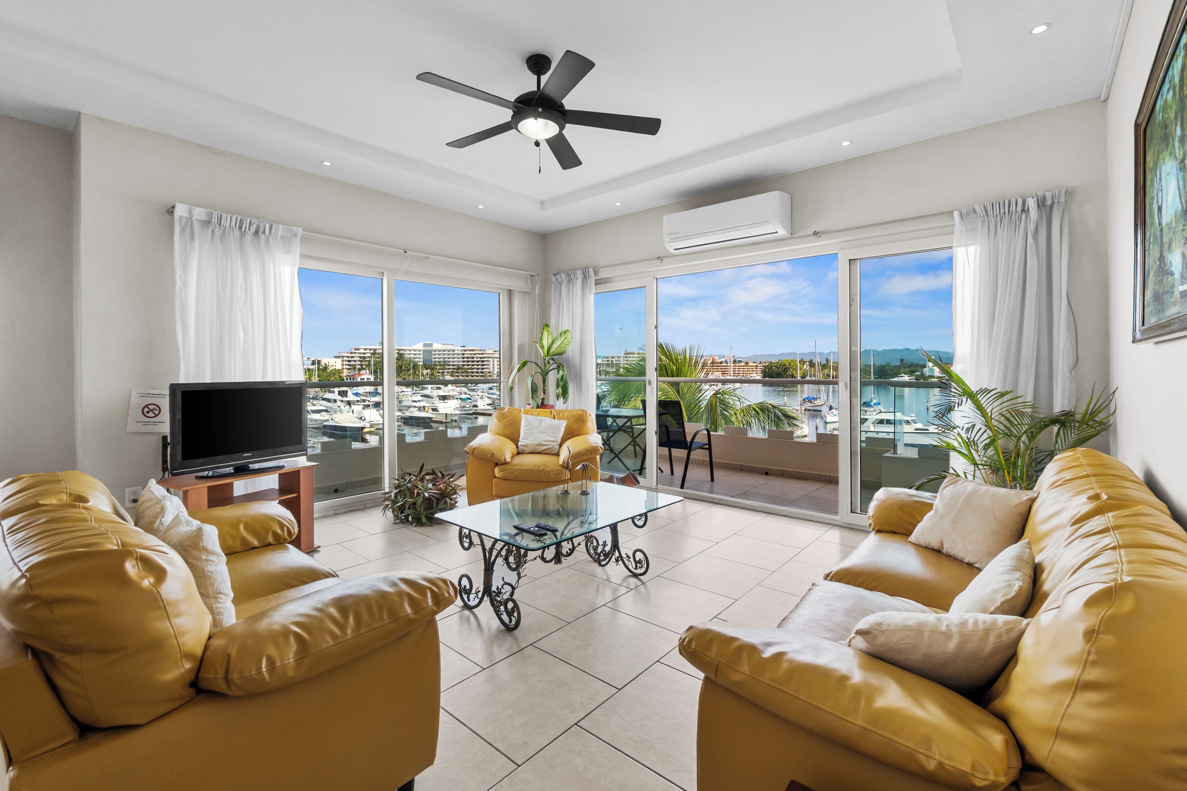 Un salon spacieux équipé d’un téléviseur à écran plat, de deux canapés, d’une table basse en verre et d’un ventilateur de plafond.