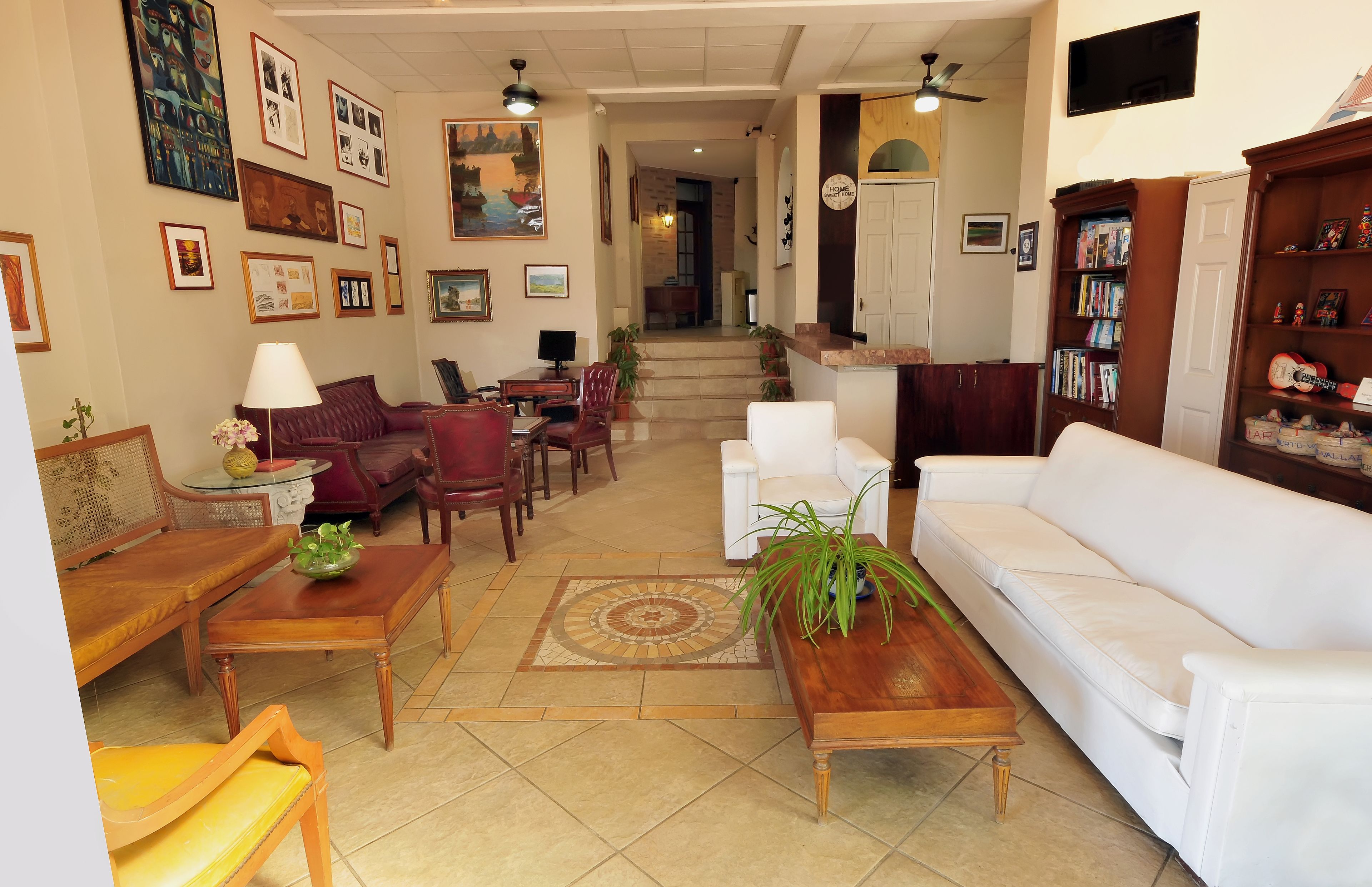 A spacious living room with a white sofa, a wooden coffee table, and a red armchair. There are framed pictures on the walls and a bookshelf filled with books.