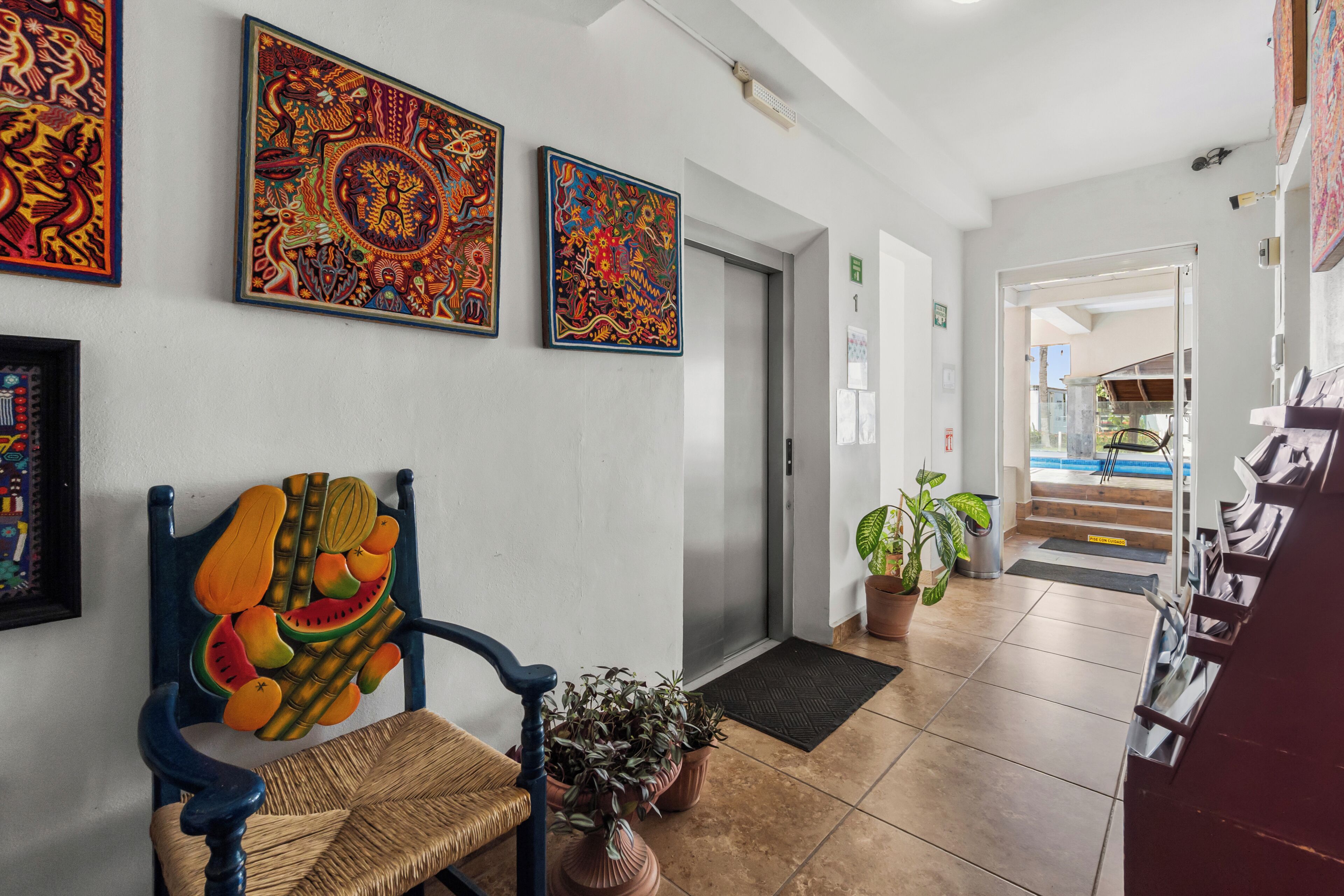 Un vestíbulo de hotel con una recepción, una silla con respaldo colorido y dos grandes cuadros en la pared.