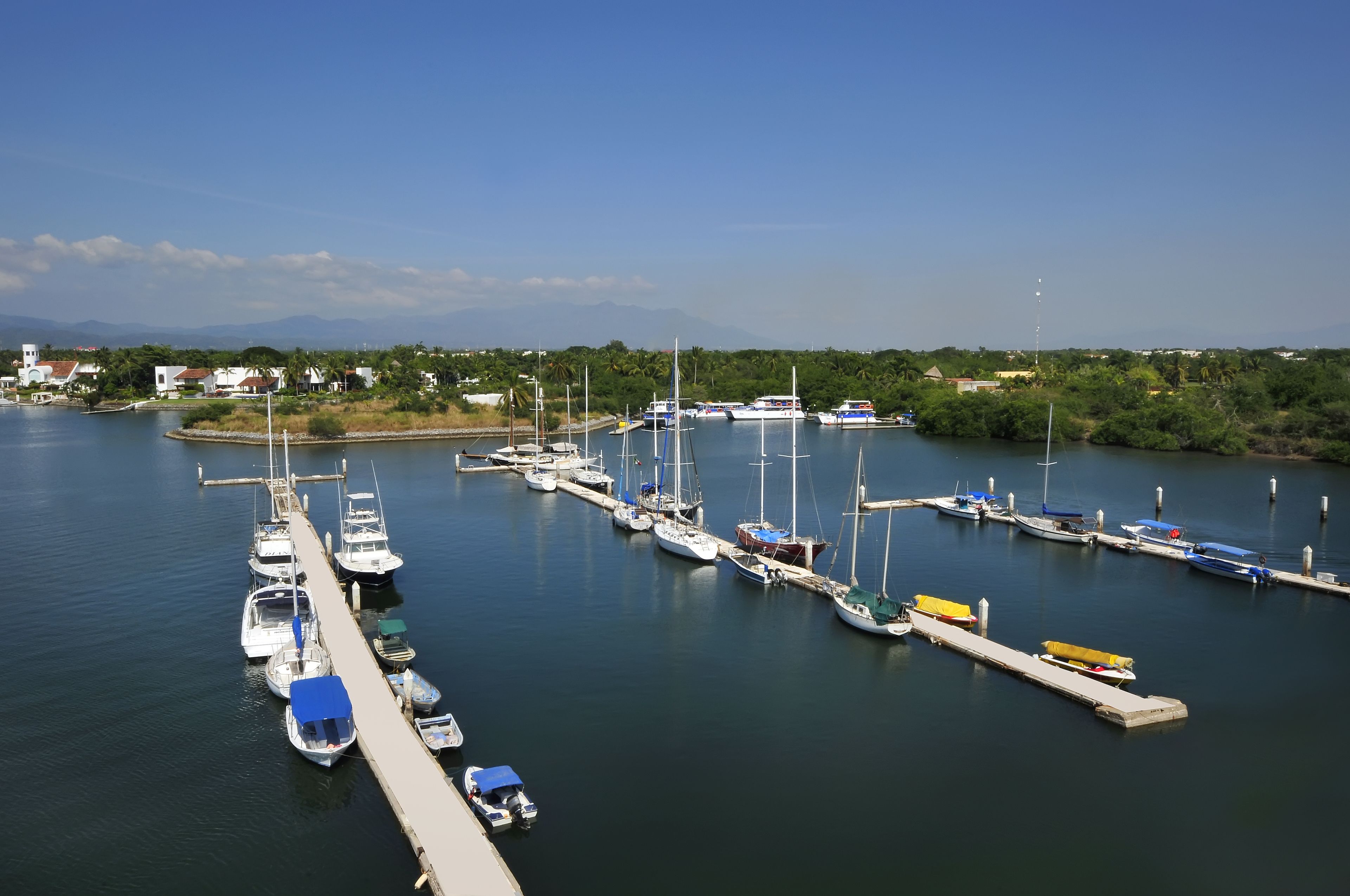 A marina with boats docked along piers, surrounded by greenery and distant mountains.