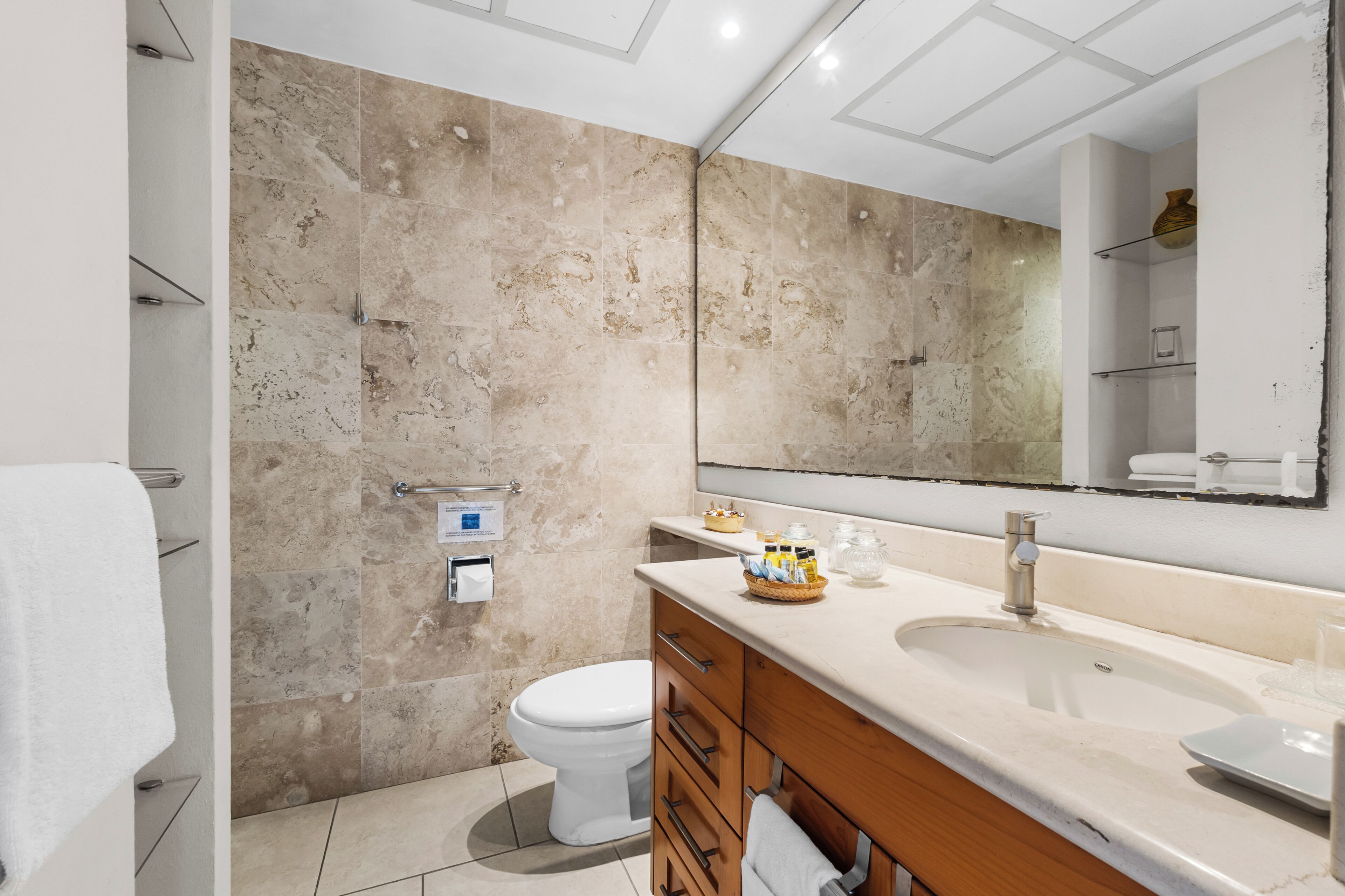 Un baño moderno con un espejo grande, inodoro, lavamanos y tocador con cajones.