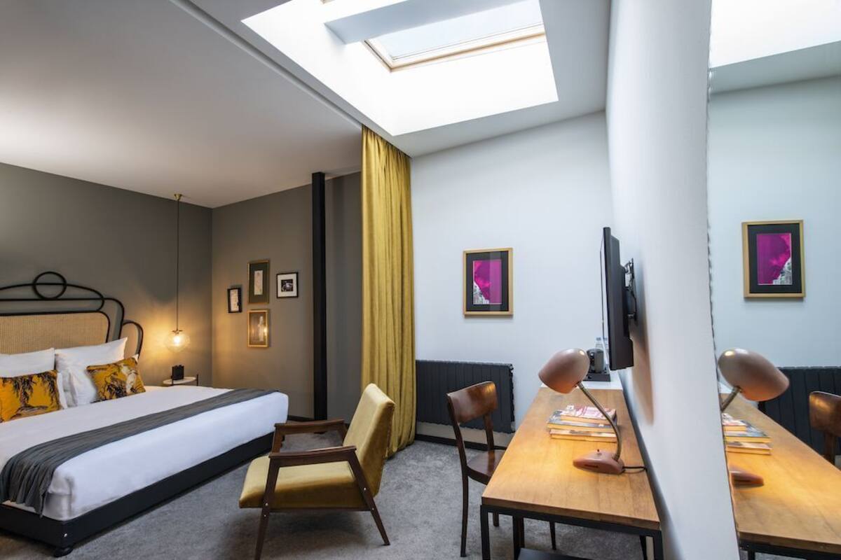 A hotel room with a bed, a desk, a chair, a TV, and framed pictures on the wall.