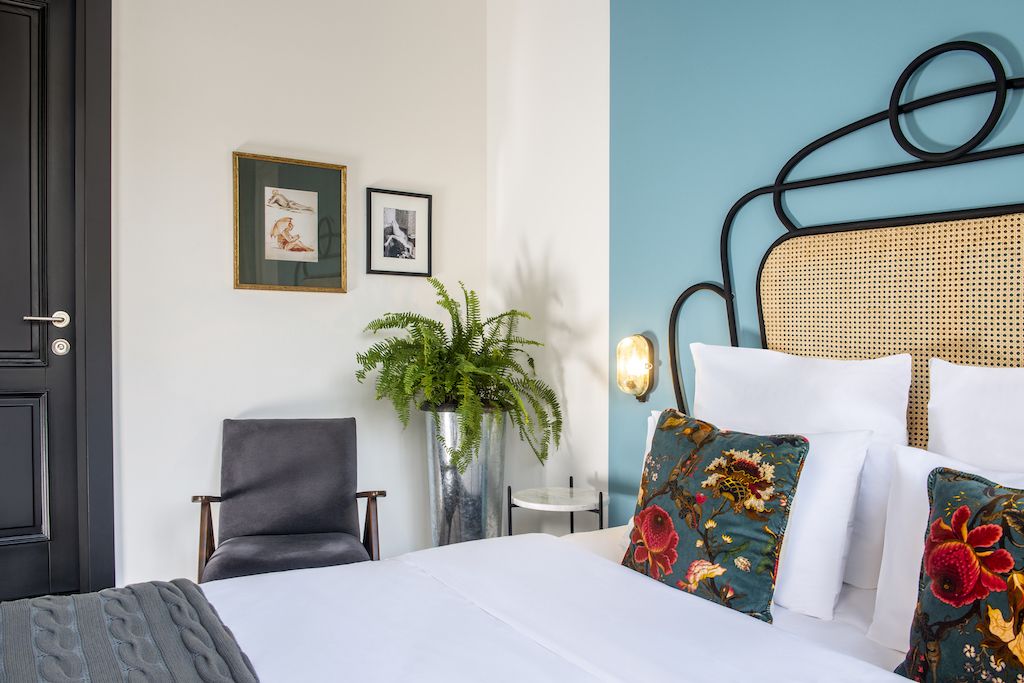 Quarto de hotel com cama, cadeira, mesinha e planta em vaso.