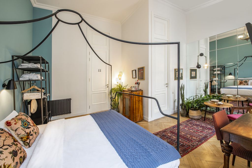Un dormitorio con una cama con dosel, un aparador de madera, un espejo y un rincón comedor con una mesa y sillas.