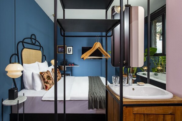 Un dormitorio con cama, mesita de noche, lámpara y un perchero de madera.