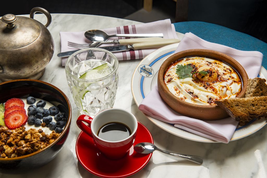 Ein Tisch mit einer Joghurt-Schale, belegt mit Erdbeeren und Blaubeeren, einer Kaffeetasse, einer Suppenschale und einem Teekännchen.