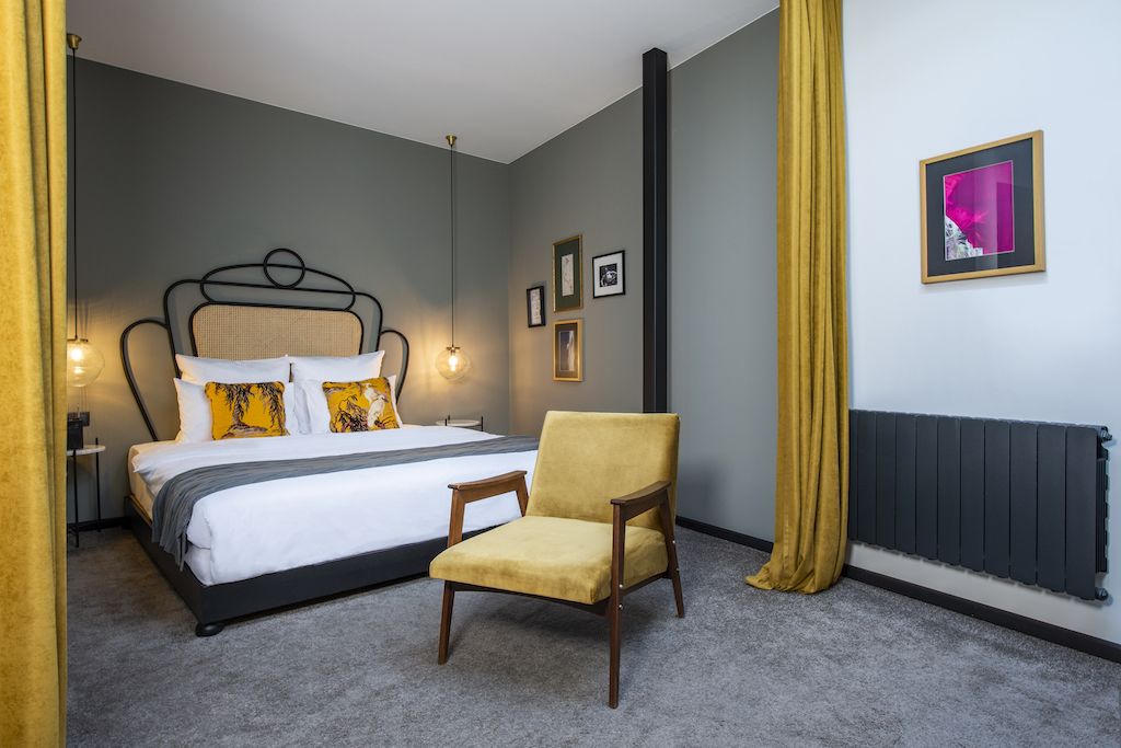 A bedroom with a bed, a chair, a radiator, and framed pictures on the wall.