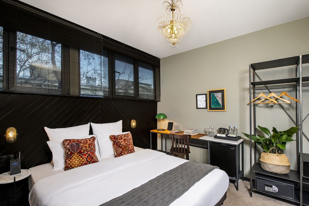 A modern hotel room with a large bed, a desk, a wardrobe, and a chandelier.