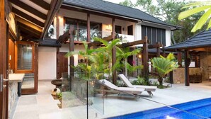 Une maison moderne dotée d’une piscine, de balustrades en verre et de plantes tropicales.