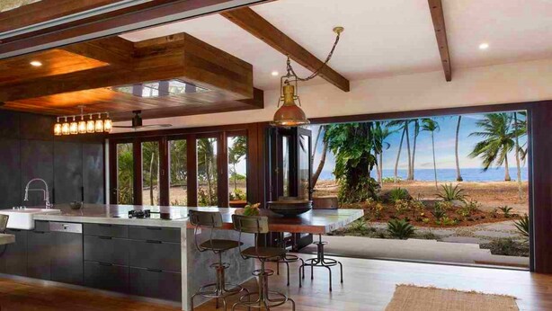 Une cuisine moderne dotée d’un grand îlot central, de tabourets de bar et offrant une vue sur la plage.