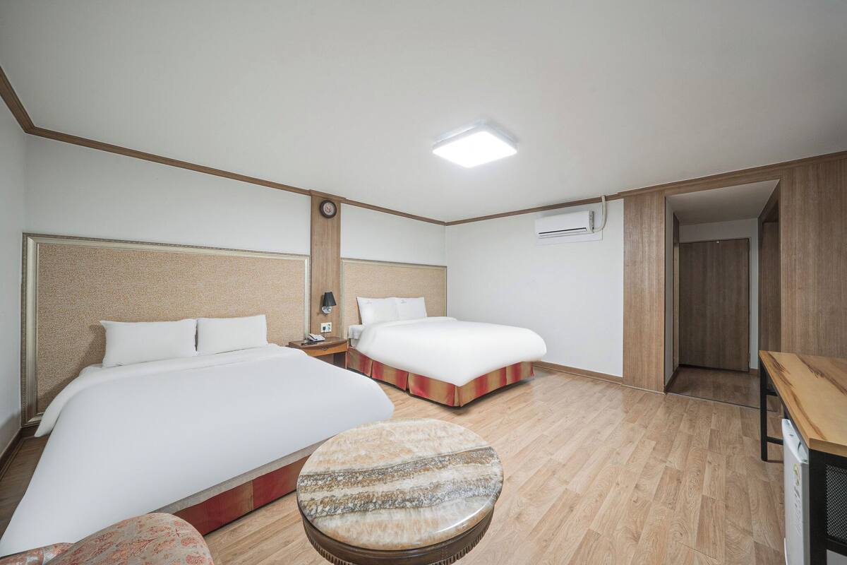 A hotel room with two beds, a round table, a nightstand, and a wooden floor.