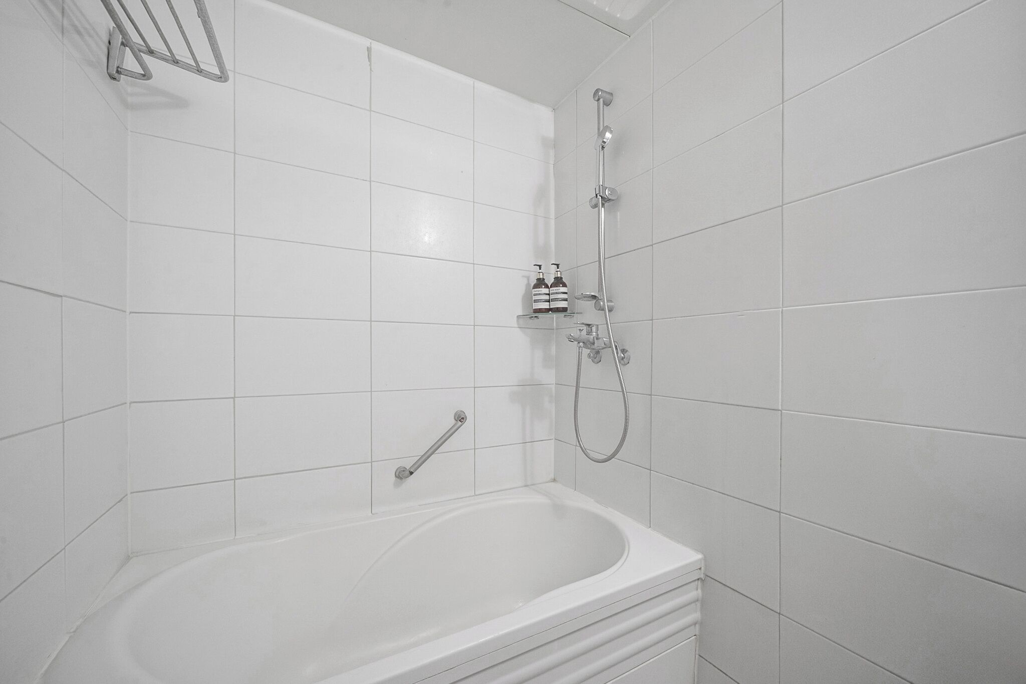 A modern bathroom with a white bathtub, a handheld showerhead, and a built-in faucet.