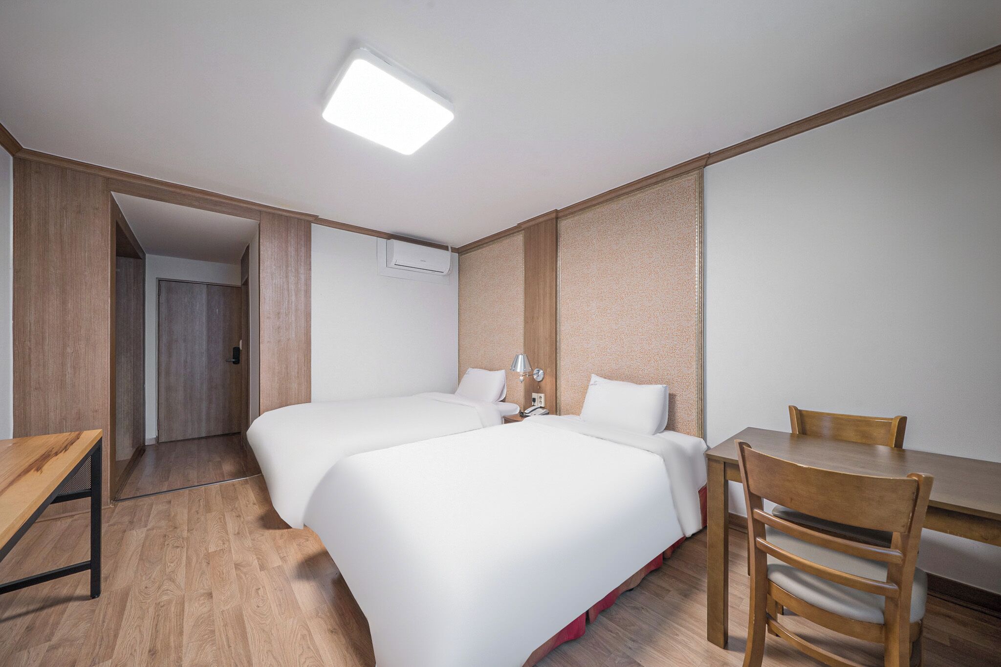 A hotel room with two beds, a wooden desk, a chair, and a small table.