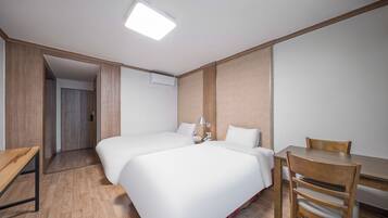 A hotel room with two beds, a wooden desk, a chair, and a small table.