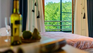 Un dormitorio con cama, una ventana con cortinas, una botella y un cuenco con fruta.