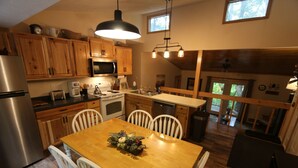 A kitchen with wooden cabinets, a stainless steel refrigerator, a microwave, and a dining table with chairs. - Beautifully Wooded & Serene Setting (Hot Tub) (Maggie Valley)