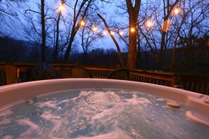 A hot tub surrounded by a wooden deck with string lights, trees, and a view of the sky. - Beautifully Wooded & Serene Setting (Hot Tub) (Maggie Valley)