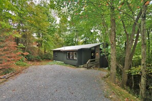 Une petite cabane avec une allée en gravier, entourée d’arbres et de feuillage.