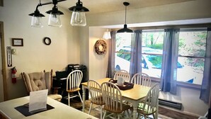 A dining area with a wooden table and chairs, a kitchen with a sink, and a window with curtains. - Beautifully Wooded & Serene Setting (Hot Tub) (Maggie Valley)