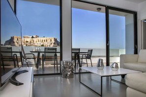 A modern hotel room with a balcony, a dining area, and a view of ancient ruins.