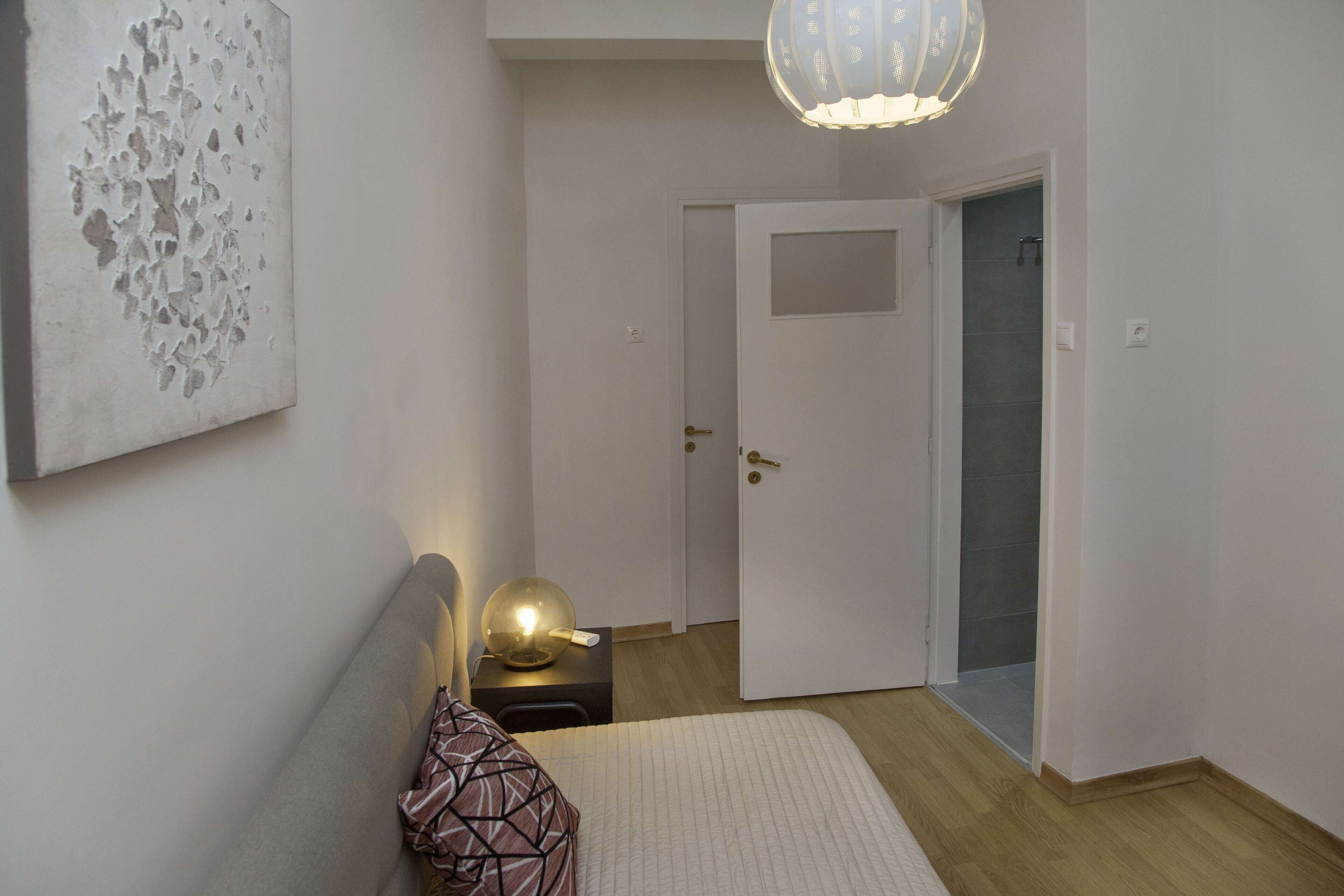 Una camera da letto con un letto, un comodino, una lampada e una porta che dà su un bagno.