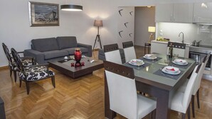 A modern living room with a sofa, dining table, and chairs. There is a kitchen area with cabinets and a sink. - Exceptional Penthouse near Acropolis Museum by GHH (Athens)