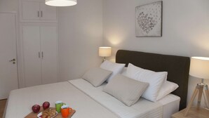 A neatly made bed with pillows and a bedside table with a lamp. There is a plate with apples and croissants on the bed. - Exceptional Penthouse near Acropolis Museum by GHH (Athens)
