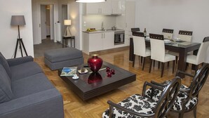 A modern living room with a grey sofa, a coffee table with decorative items, and a dining area with white chairs and a table. - Exceptional Penthouse near Acropolis Museum by GHH (Athens)