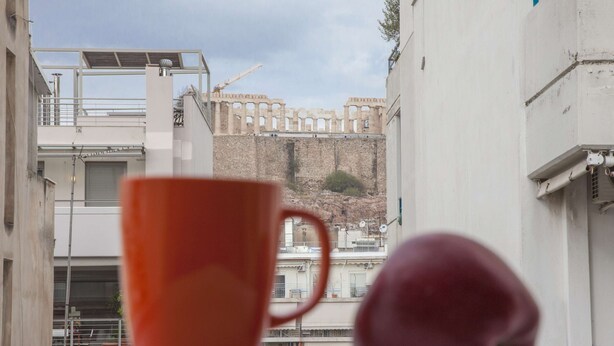 A red cup and a peach on a balcony overlooking a construction site with a white building in the background. - Exceptional Penthouse near Acropolis Museum by GHH (Athens)