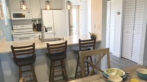 Una cocina moderna con armarios blancos, una isla central con taburetes y una mesa de comedor con fuentes y vasos.