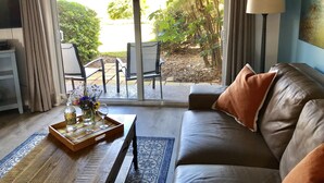 Una sala de estar con un sofá, una mesa de centro con una bandeja de bebidas, un televisor y vistas al exterior a través de un ventanal.