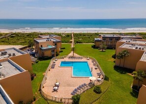 A resort with a central swimming pool surrounded by lounge chairs, a view of the beach, and a clear sky. - Large 1BD, 1BA Ocean Front Complex, Ground Floor, Free Wifi, Hdtv, Large pool (St Augustine)
