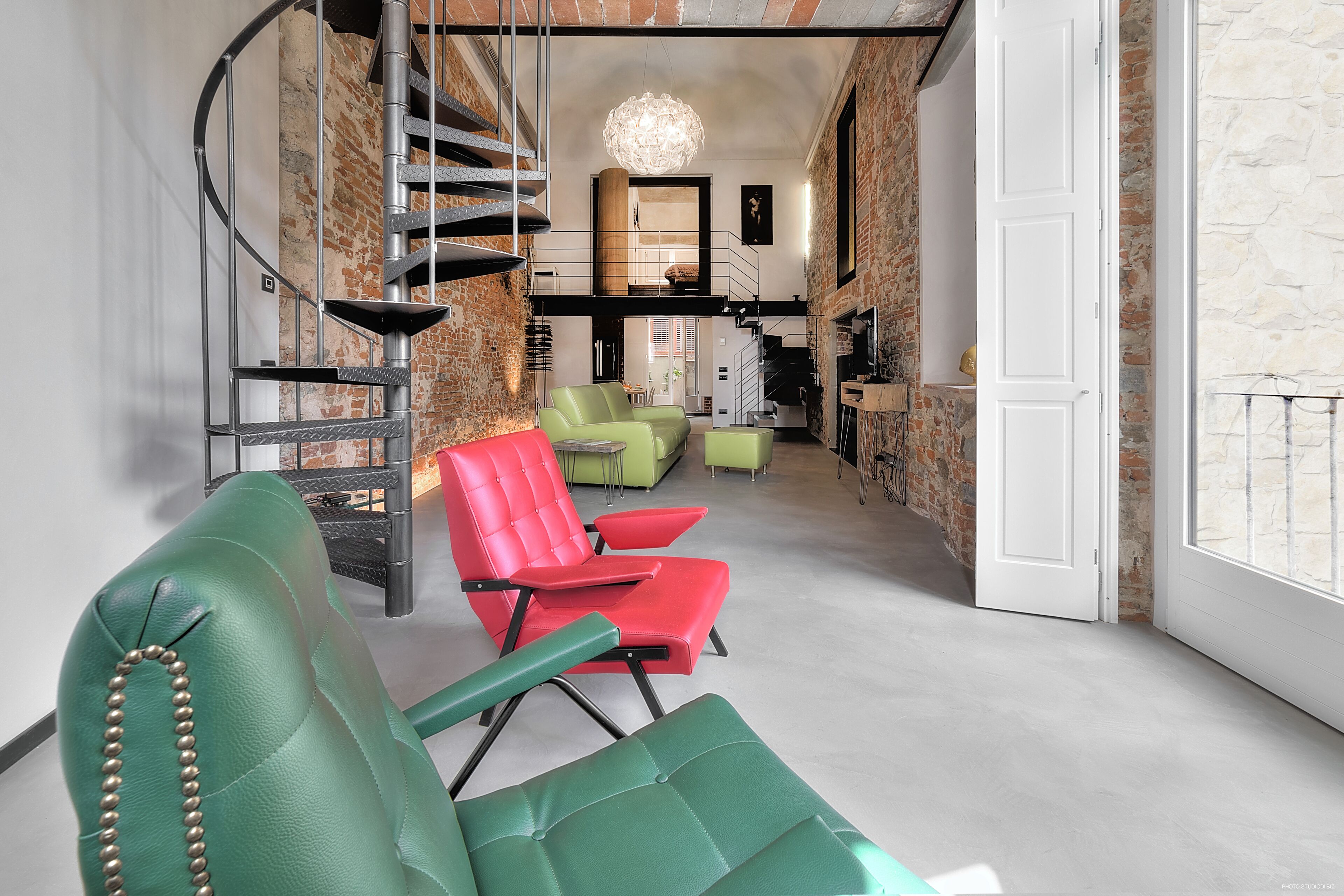 Un interior modern amb una escala de caragol, cadires verdes i vermelles, i una paret de pedra.