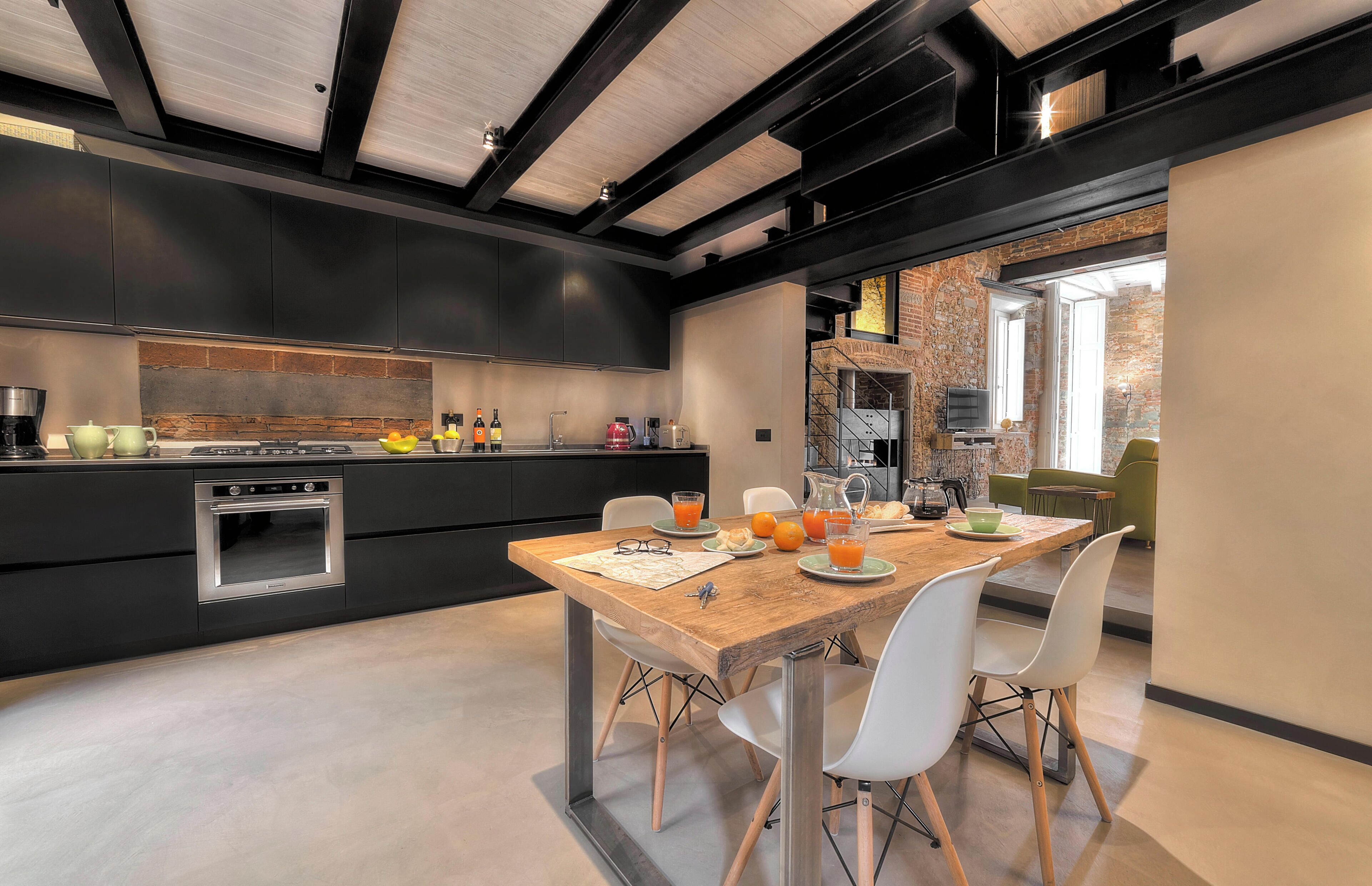 Una cocina moderna con armarios oscuros, una mesa de comedor de madera y sillas blancas.