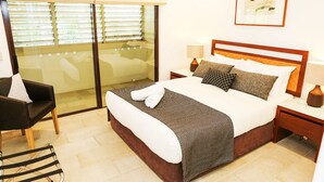 Une chambre d’hôtel avec un lit, une chaise, une table de chevet, une lampe et une fenêtre avec des stores.