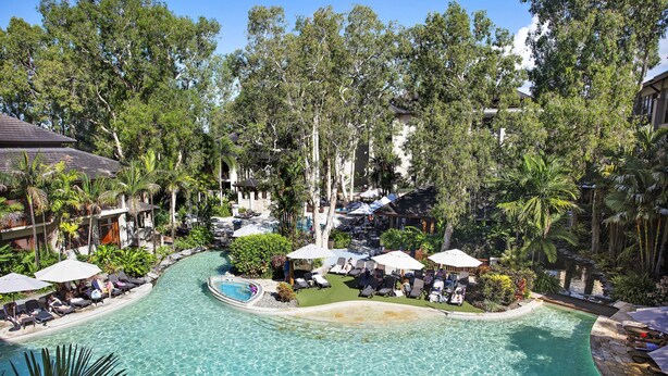 Un complexe hôtelier doté d’une piscine entourée de chaises longues et de parasols, situé dans un environnement tropical caractérisé par une végétation luxuriante.