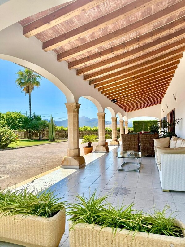 A covered outdoor patio with a wooden ceiling, stone columns, and potted plants.