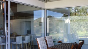 A modern outdoor dining area with a wooden table and chairs, large glass sliding doors, and a view of the garden. - 4 bedroom house with private pool (Celorico de Basto)