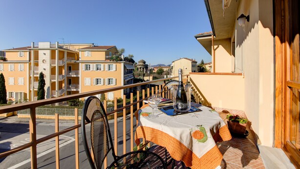 Un balcon avec une table dressée pour deux personnes, donnant sur un quartier résidentiel avec ses immeubles et un ciel dégagé.