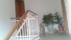 Un escalier doté d’une main courante en bois et de balustres blanches, menant à un palier agrémenté de plantes en pot et d’un vase décoratif.
