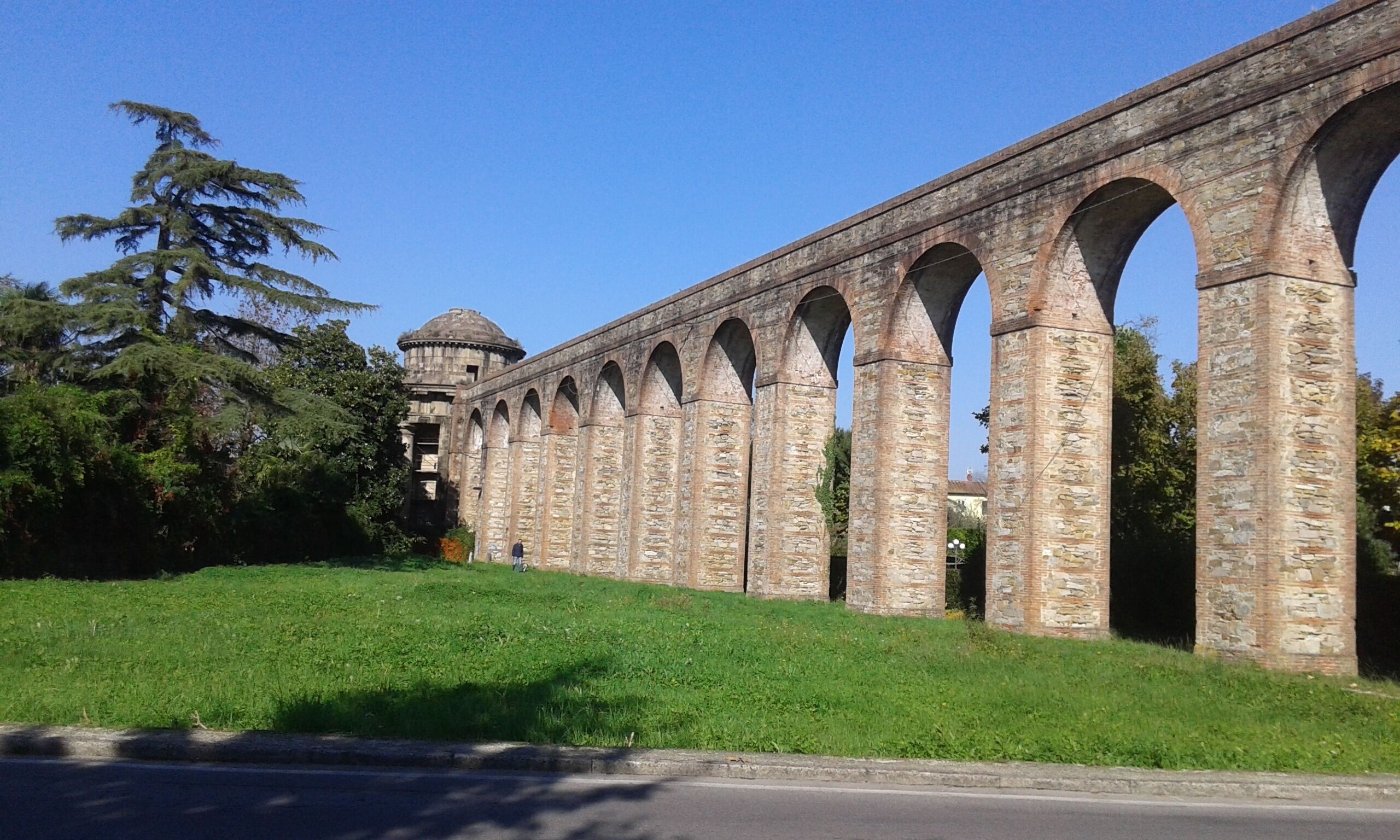 A stone bridge with multiple arches, a grassy embankment, and a dome structure in the background.