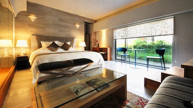 Een moderne hotelkamer met een groot bed, een glazen salontafel, een bank en uitzicht op groen door het raam.