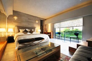 Een moderne hotelkamer met een groot bed, een glazen salontafel, een bank en uitzicht op groen door het raam.