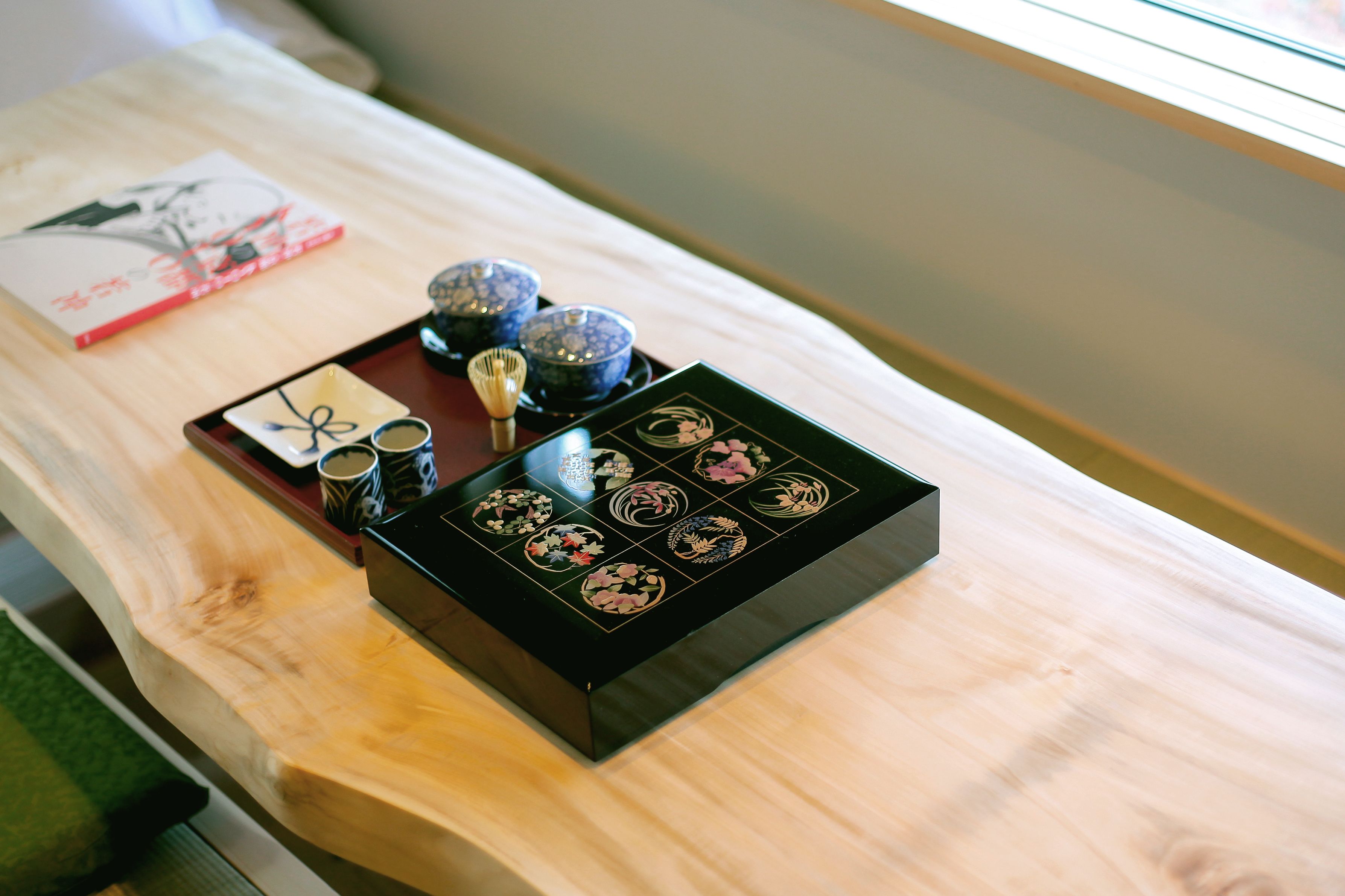 A wooden table with a black tray holding various items including a book, a whisk, and several small containers.