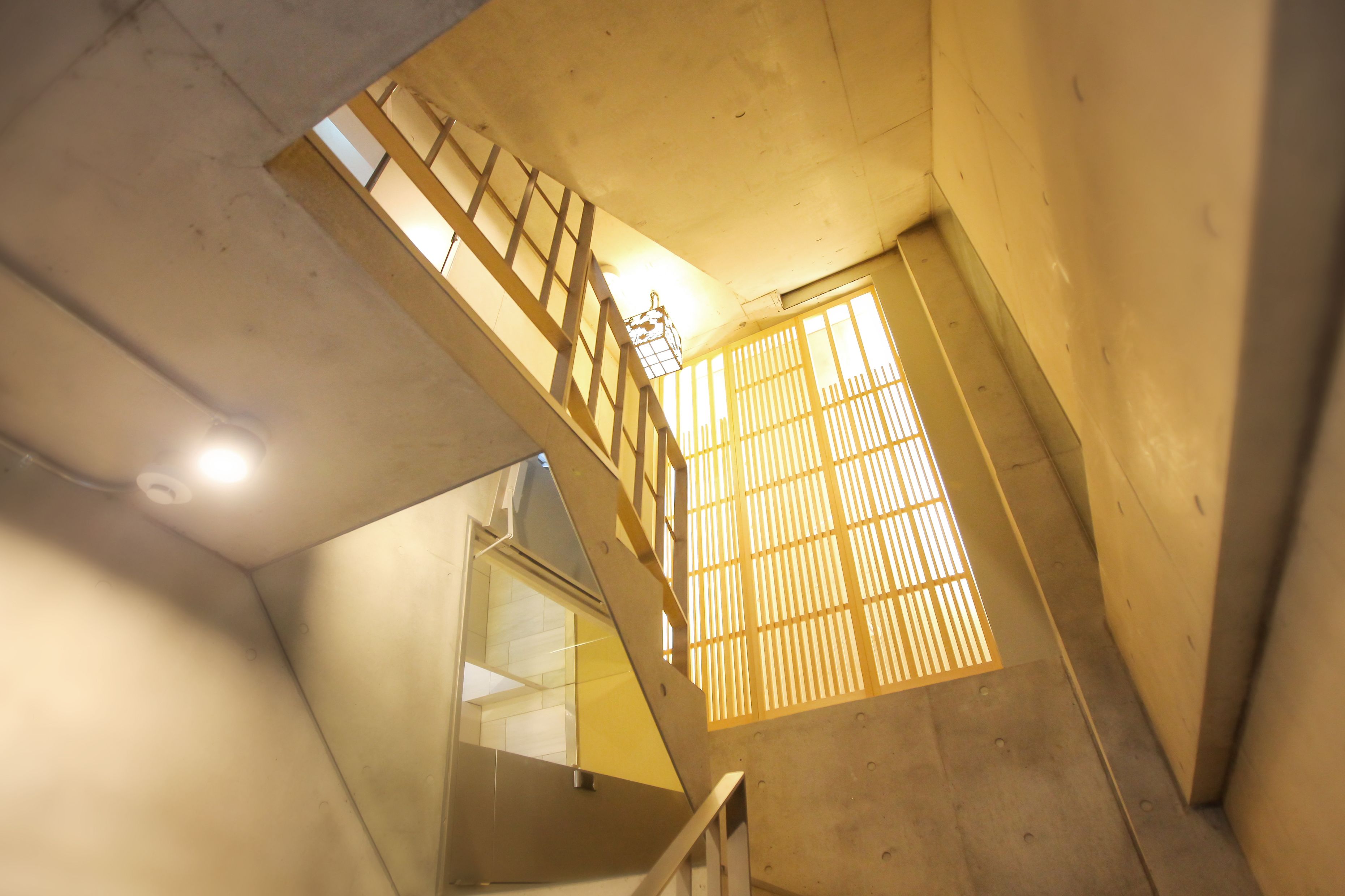 Un escalier avec une rampe en bois et une fenêtre équipée de stores verticaux.