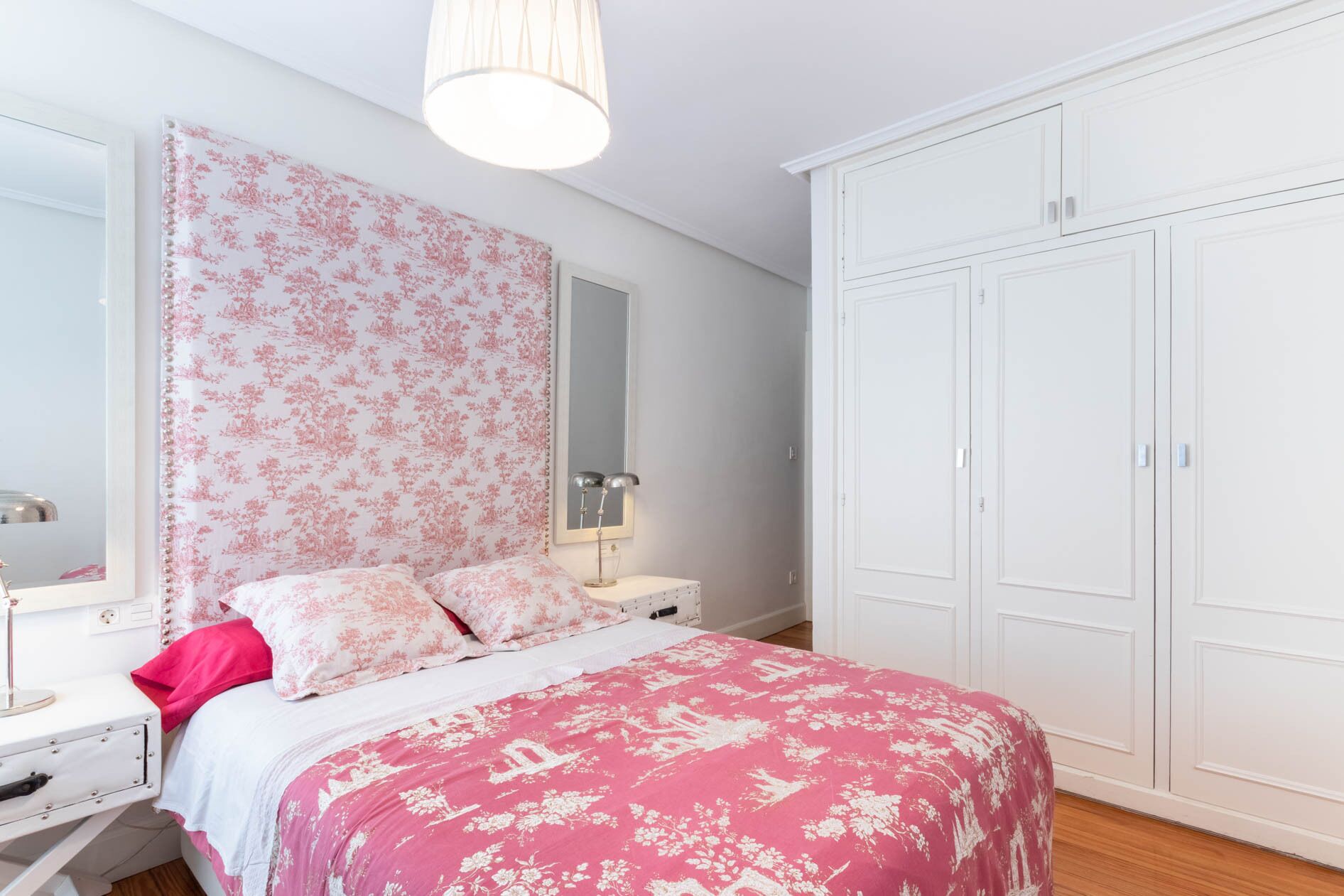 Een slaapkamer met een bed, nachtkastje, dressoir, kledingkast en spiegel.