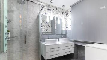 Un baño moderno con cabina de ducha de vidrio, dos lavamanos, un espejo grande y un inodoro.