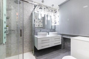 Un baño moderno con cabina de ducha de vidrio, dos lavamanos, un espejo grande y un inodoro.